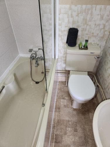 A compact bathroom featuring a bathtub, toilet, and tiled walls exudes a practical and cozy atmosphere, ideal for travelers seeking efficient space utilization in accommodations.