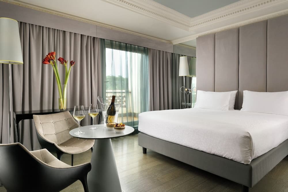 A serene hotel room features a cozy bed, modern furnishings, and a balcony view, ideal for travelers seeking relaxation and comfort.