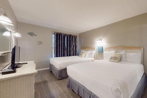 A cozy hotel room features two neatly made beds with white linens, a desk with a computer, patterned curtains, and soft lighting, ideal for travelers seeking comfort and convenience.