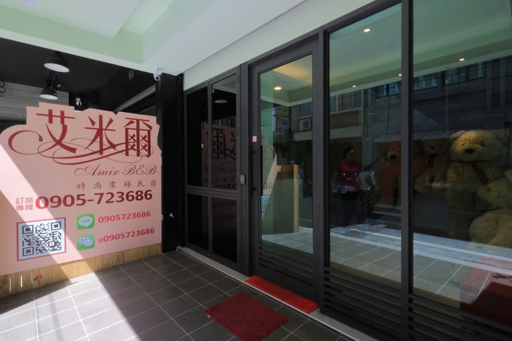 A cozy boutique B&B entrance features a stylish signboard with contact details, glass doors, and plush teddy bears in the window, inviting travelers seeking a charming urban retreat.