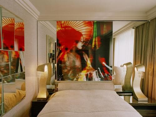 A cozy hotel room features a plush bed adorned with a vibrant, artistic wall mural, mirrored accents, and soft lighting, creating an inviting atmosphere ideal for travelers seeking comfort and style.