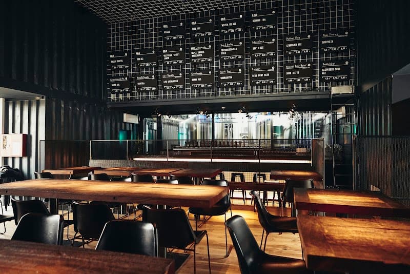 A cozy, modern brewery interior features wooden tables, sleek black chairs, and an illuminated beer menu board, creating an inviting atmosphere perfect for craft beer enthusiasts exploring Berlin's vibrant nightlife.