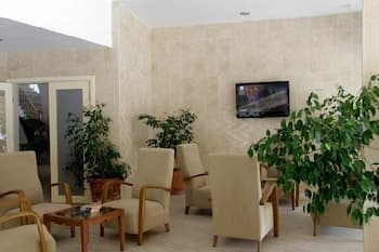 A cozy lounge area with beige armchairs, green potted plants, and a wall-mounted TV creates a serene atmosphere ideal for travelers seeking relaxation in a hotel or airport waiting space.