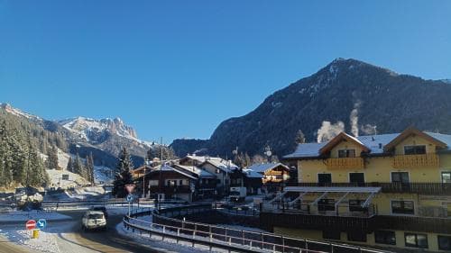 A serene winter scene captures a quaint village nestled among snow-covered mountains under a clear blue sky, featuring traditional chalets and a winding road ideal for a peaceful ski resort getaway.
