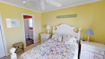 A cozy bedroom with yellow walls, a patterned bedspread, and white furniture exudes a warm and inviting atmosphere, perfect for travelers seeking a comfortable and relaxing retreat.
