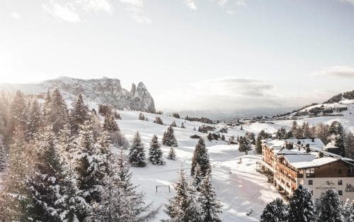 A serene winter landscape featuring snow-covered pine trees and quaint alpine buildings nestled among majestic mountains, ideal for a peaceful ski resort getaway.