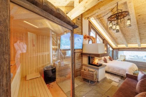 A cozy attic bedroom with wooden beams, a fireplace, and an adjacent sauna offers a serene retreat, perfect for travelers seeking relaxation in a rustic lodge setting.