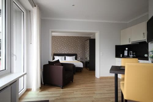 A cozy hotel suite features a neatly made bed, modern furnishings, and a kitchenette, creating a welcoming atmosphere ideal for travelers seeking comfort and convenience.
