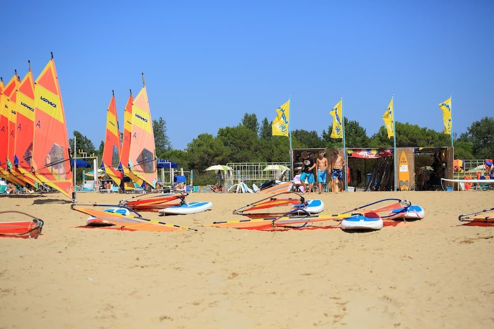 A vibrant beach scene with colorful windsurf boards lined up on the sand under clear blue skies, surrounded by lush greenery and flags, perfect for an adventurous summer getaway.
