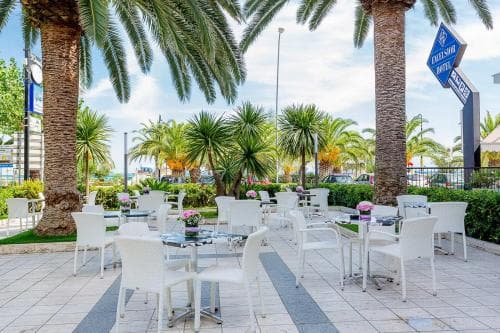 A serene outdoor café with white tables and chairs nestled among lush palm trees under a clear blue sky, ideal for travelers seeking a relaxing tropical retreat.
