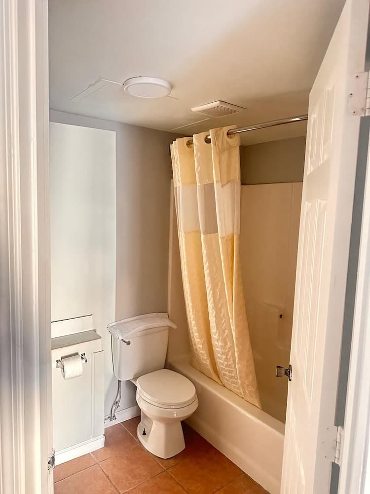 A cozy bathroom with a yellow shower curtain, white toilet, tiled floor, and frosted glass window creates a serene atmosphere ideal for travelers seeking comfort in compact spaces.