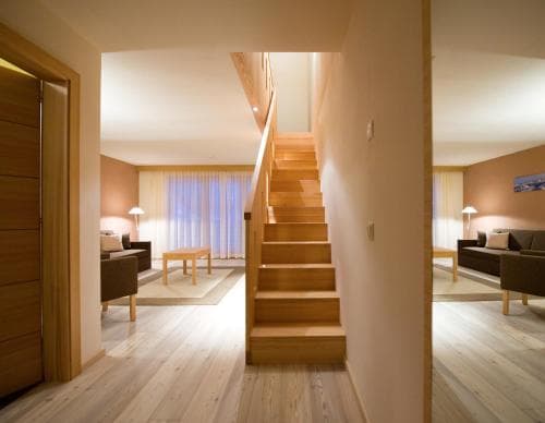 A cozy modern apartment features warm wooden stairs leading to an upper level, with inviting living spaces on either side, ideal for travelers seeking comfort and style in their accommodations.