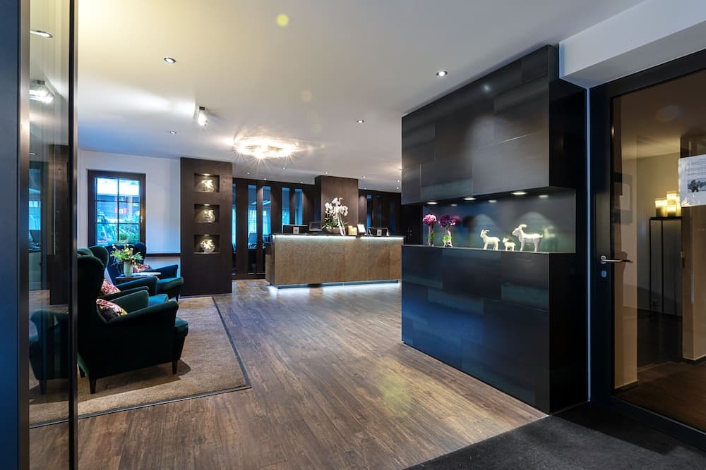 A modern hotel lobby exudes elegance with sleek wooden floors, plush green armchairs, a stylish reception desk, and decorative shelving, ideal for travelers seeking a luxurious stay experience.