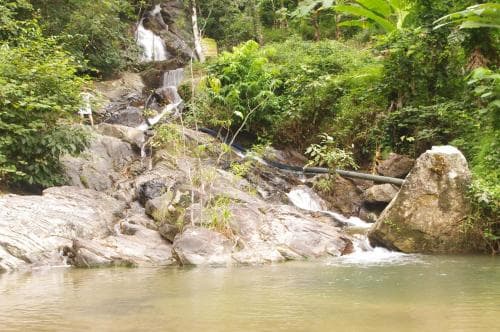 A serene tropical waterfall cascades over rocky terrain surrounded by lush greenery, creating an ideal spot for nature photography and tranquil hiking adventures.
