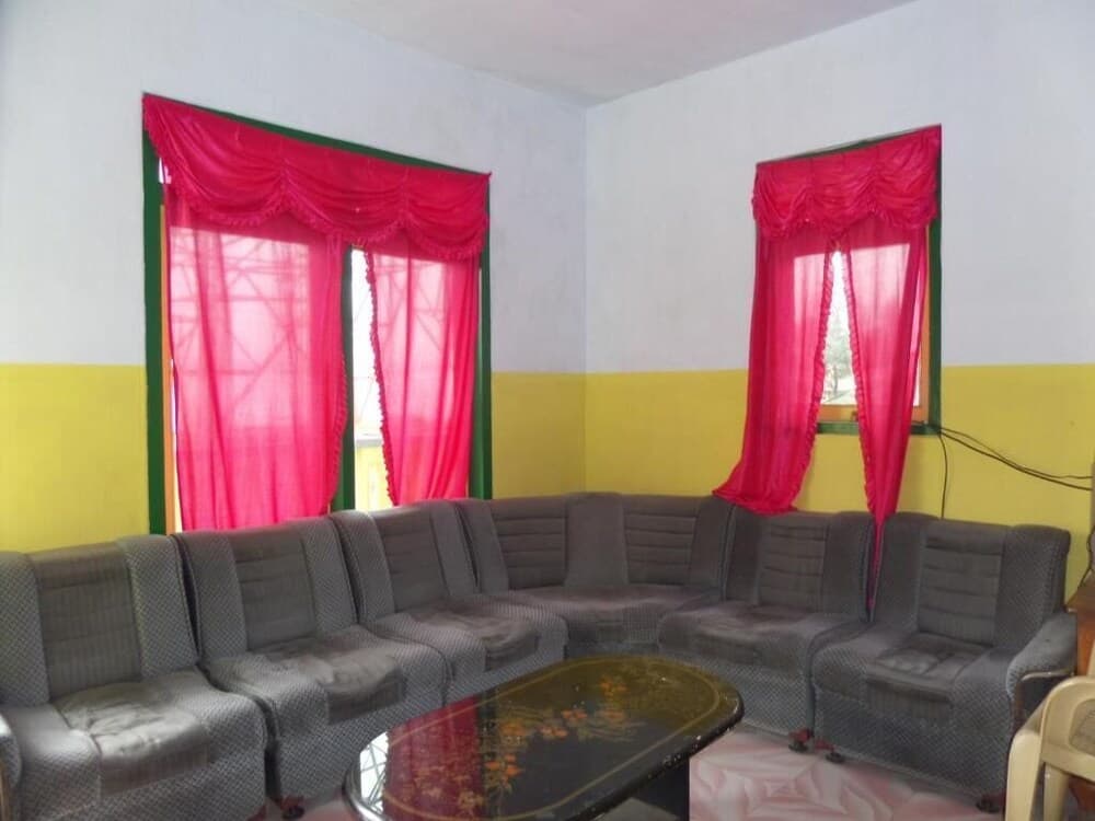 A cozy living room with vibrant yellow walls, bold red curtains, and a large sectional sofa creates a warm and inviting atmosphere, ideal for travelers seeking a comfortable stay in a homely environment.