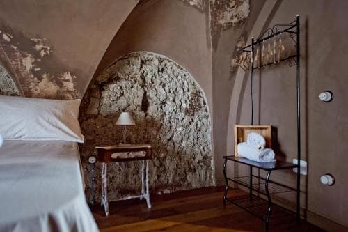 A cozy bedroom with rustic charm features an arched stone wall, wooden furniture, and soft lighting, ideal for travelers seeking a serene and historic accommodation experience.