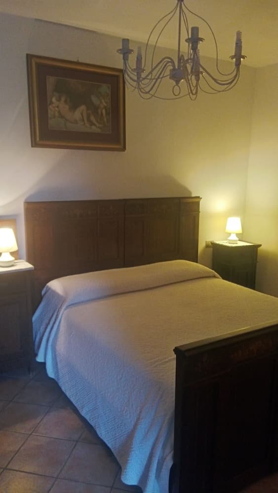 A cozy bedroom with warm lighting features a wooden bed adorned with a white quilt, flanked by nightstands with lamps, under a vintage chandelier, ideal for travelers seeking a charming and intimate accommodation experience.