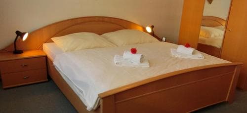 A cozy hotel room features a neatly made bed with white linens, wooden furnishings, and a warm ambiance, ideal for travelers seeking comfort and relaxation.
