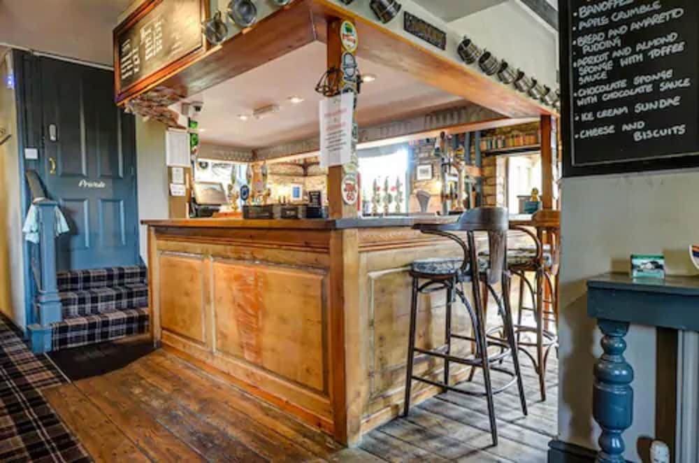 A cozy pub interior with wooden floors, rustic bar counter, plaid seating, and a menu chalkboard exudes warmth and charm, perfect for travelers seeking a traditional drinking spot with hearty desserts.