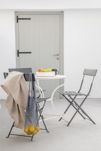 A minimalist outdoor patio features a white table set with fresh fruit, surrounded by metal chairs, evoking a serene and stylish vibe perfect for a relaxing retreat or home decor inspiration.