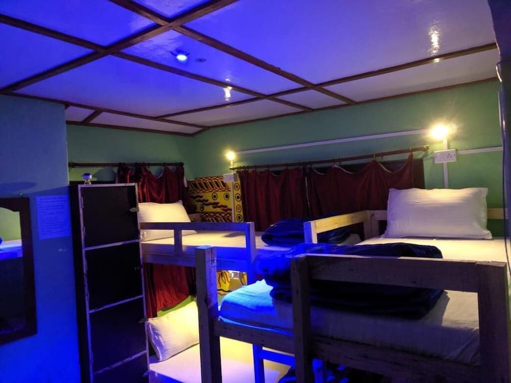 A cozy hostel room with bunk beds, green walls, and ambient blue lighting creates a relaxed atmosphere ideal for budget travelers seeking comfort and camaraderie.
