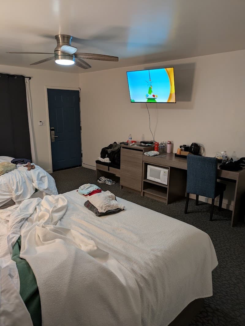 A cozy motel room in Kings Beach features comfortable beds, a mounted TV displaying vibrant colors, a desk with a microwave, and a ceiling fan, ideal for travelers seeking relaxation near Lake Tahoe.