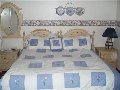 A cozy bedroom with a neatly made bed adorned in blue floral patterns, wooden furniture, and decorative plates on the wall, evokes a serene and inviting atmosphere ideal for travelers seeking a peaceful retreat.