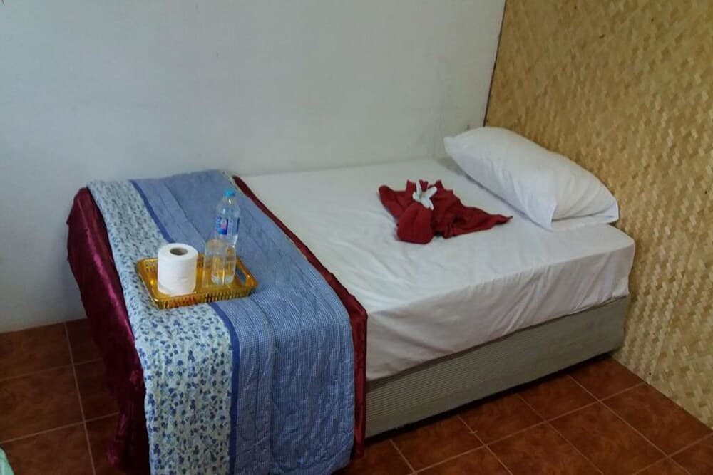 A cozy budget-friendly hotel room features a neatly made bed with a blue patterned blanket, a tray holding toiletries, and a bamboo-textured wall, ideal for travelers seeking simple accommodations.