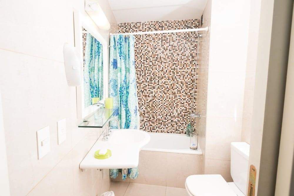 A cozy bathroom features a mosaic-tiled shower wall, a colorful sea-themed curtain, and a compact sink setup, ideal for travelers seeking a clean and cheerful accommodation space.