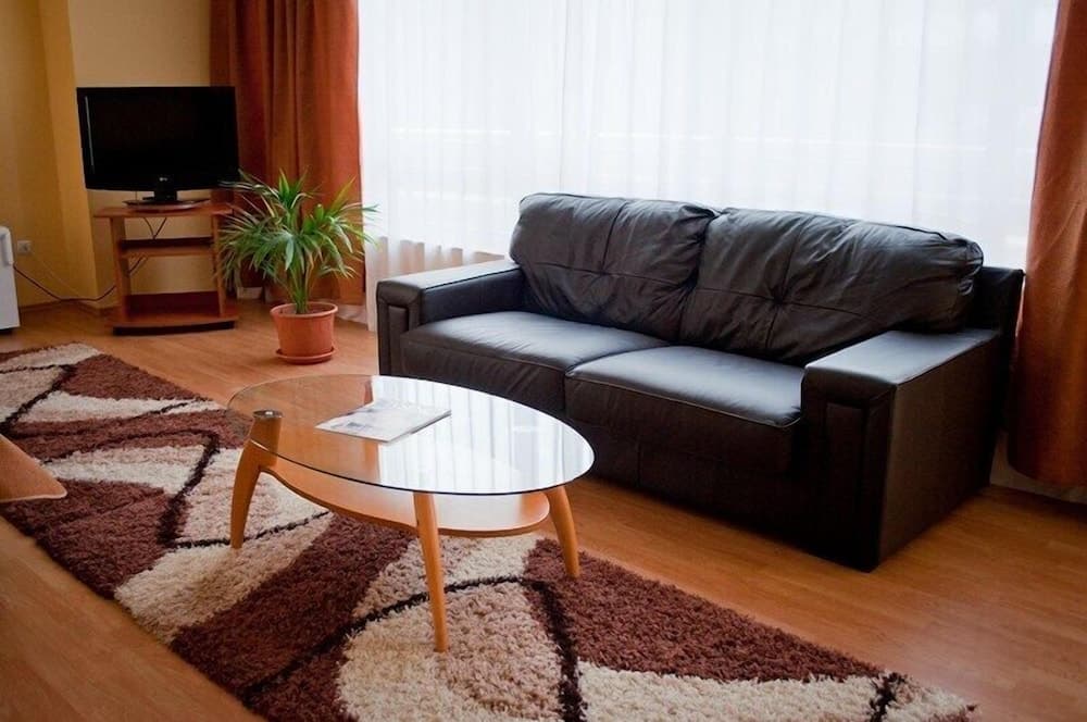 A cozy living room with a black leather sofa, wooden coffee table, patterned rug, and potted plant creates a warm and inviting atmosphere, ideal for travelers seeking comfortable accommodation.