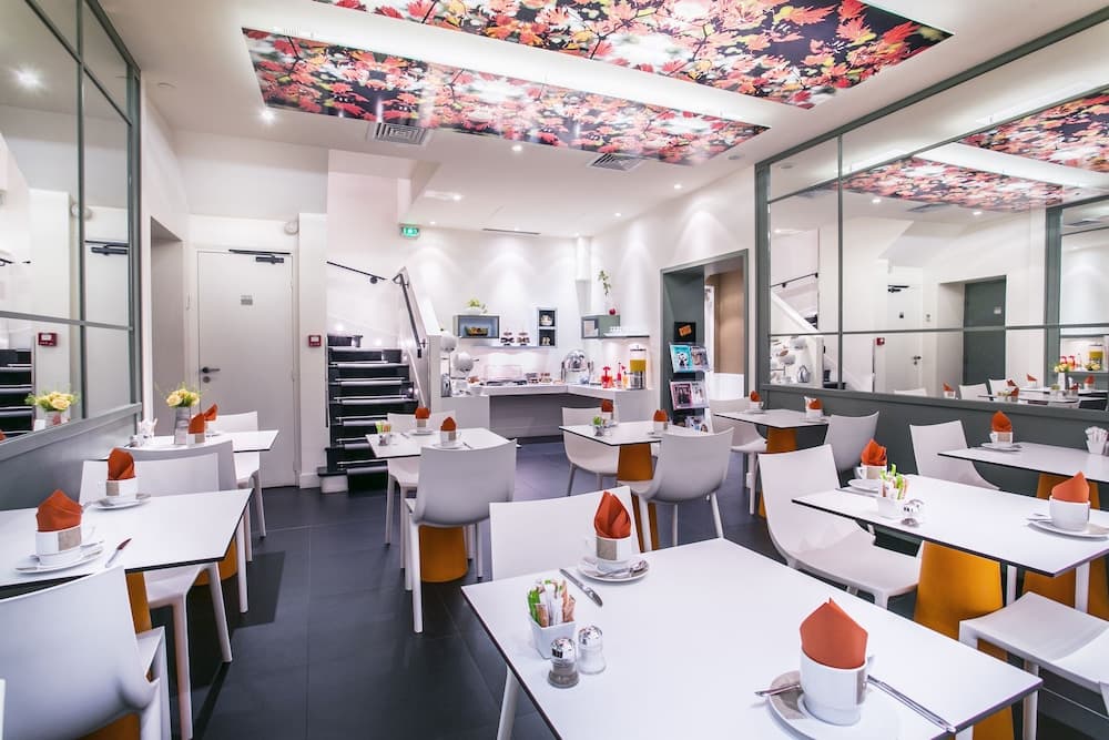 A cozy modern café with white tables, orange napkins, and autumn-themed ceiling decor offers a serene dining experience ideal for travelers seeking a stylish yet comfortable spot to relax and enjoy meals.