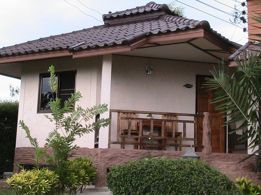 A serene tropical villa with a tiled roof, wooden porch furniture, lush greenery, and a welcoming ambiance is ideal for a peaceful vacation retreat.