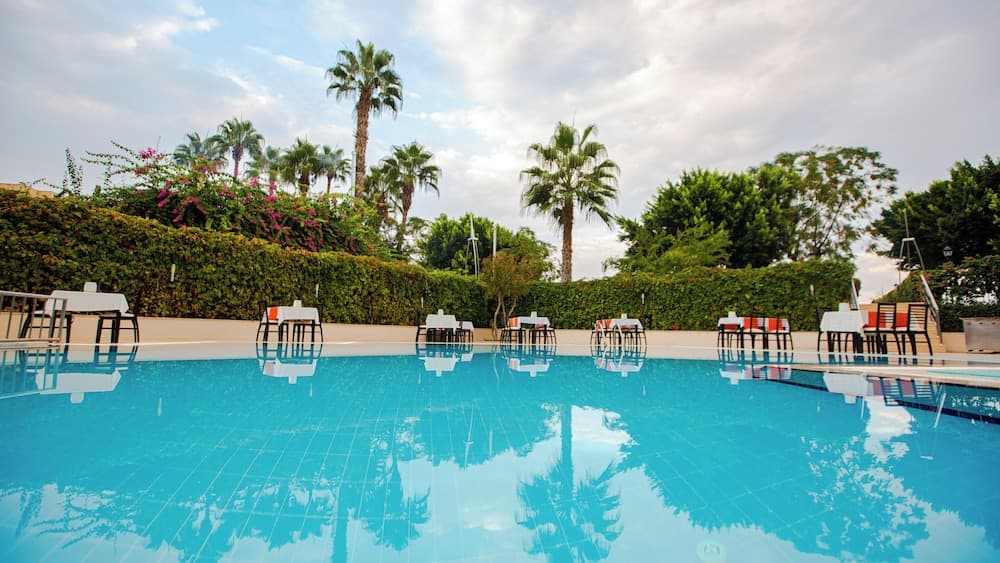 A serene resort poolside scene features calm blue waters reflecting palm trees and lounge tables, ideal for relaxing vacations in tropical destinations.