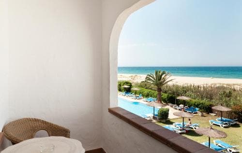 A serene balcony view captures a tranquil beachside resort scene with lounge chairs, umbrellas, and a palm tree, ideal for relaxing getaways.
