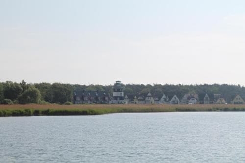 A serene lakeside view showcases quaint houses nestled among greenery under a clear sky, ideal for a peaceful getaway or vacation rental listing.
