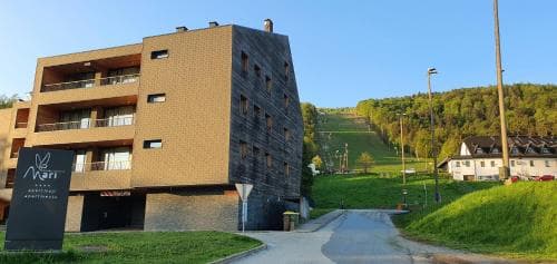 A modern hotel building stands against a serene backdrop of lush green hills under a clear blue sky, ideal for travelers seeking relaxation in a tranquil countryside setting.