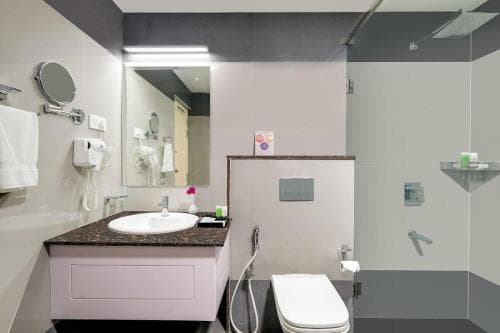 A modern hotel bathroom features sleek surfaces, a vanity with a granite countertop, a glass-enclosed shower area, and a minimalist design ideal for travelers seeking comfort and cleanliness.