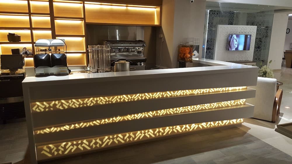 A modern hotel lobby exudes warmth with its sleek white reception desk adorned with glowing geometric patterns, complemented by a cozy seating area and a well-lit coffee station, ideal for travelers seeking a welcoming atmosphere.