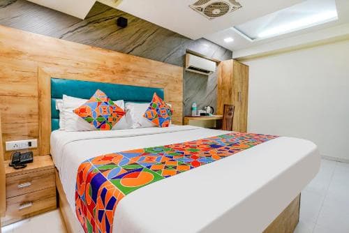 A cozy hotel room features a vibrant bedspread and pillows against a wooden headboard, creating a warm and inviting atmosphere ideal for travelers seeking comfort and style.