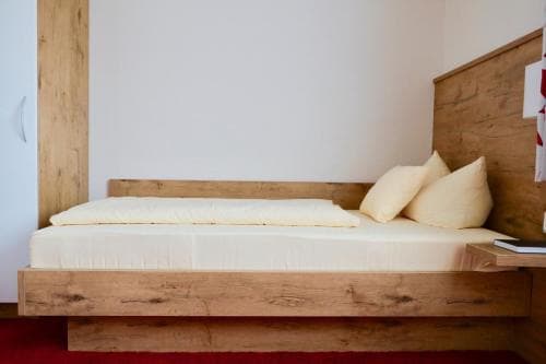 A cozy minimalist bedroom features a rustic wooden bed with white bedding, ideal for travelers seeking simplicity and comfort in a serene retreat.