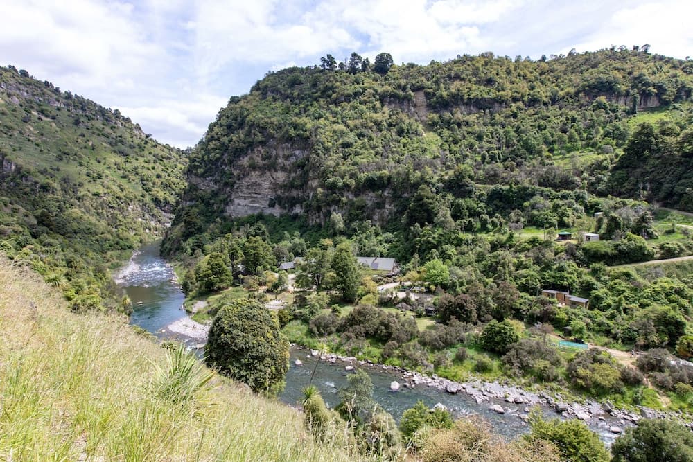 A serene river winds through lush green valleys under a partly cloudy sky, ideal for nature lovers seeking tranquil hiking trails and scenic views.