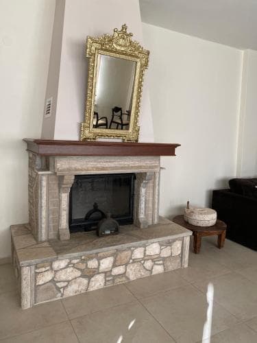 A cozy indoor setting features a rustic stone fireplace adorned with an elegant gold-framed mirror, creating a warm and inviting atmosphere ideal for a relaxing getaway or home interior inspiration.