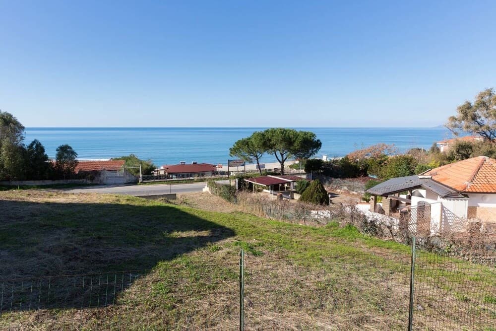 A serene coastal hillside scene with scattered houses, lush greenery, and a clear blue sea in the background, ideal for tranquil seaside retreats and property investment opportunities.