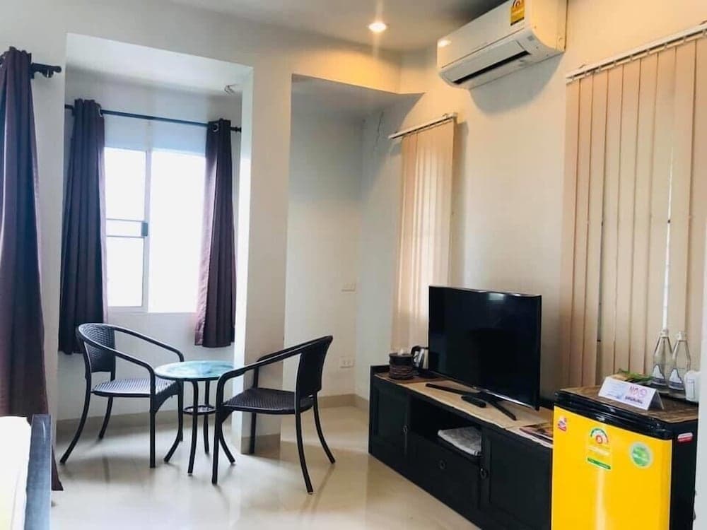 A cozy apartment living room features a small dining area by the window, a flat-screen TV on a dark cabinet, and a bright yellow mini-fridge, ideal for travelers seeking comfort and convenience in a compact space.