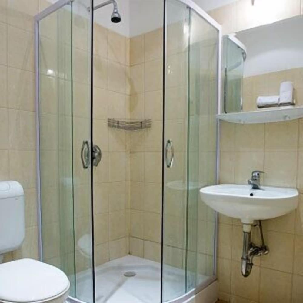A cozy hotel bathroom features a glass-enclosed shower, beige tiled walls, a white sink, and a toilet, ideal for travelers seeking cleanliness and functionality.
