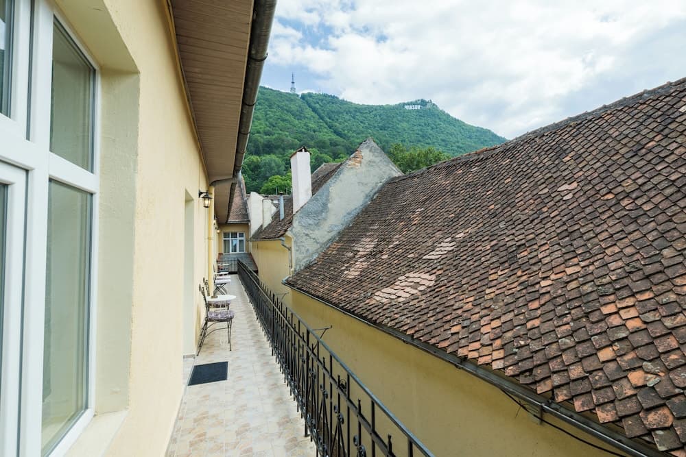 A serene balcony view of traditional tiled rooftops and lush green hills under a partly cloudy sky, ideal for travelers seeking a peaceful European retreat.