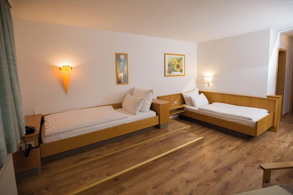 A cozy hotel room with wooden flooring, two single beds adorned with white linens, warm wall-mounted lamps, floral artwork, and a serene ambiance ideal for travelers seeking comfort and simplicity.