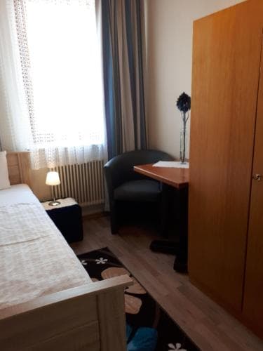 A cozy hotel room features a neatly made bed, a desk with a chair, and a window with curtains, creating a comfortable and inviting atmosphere ideal for travelers seeking relaxation.