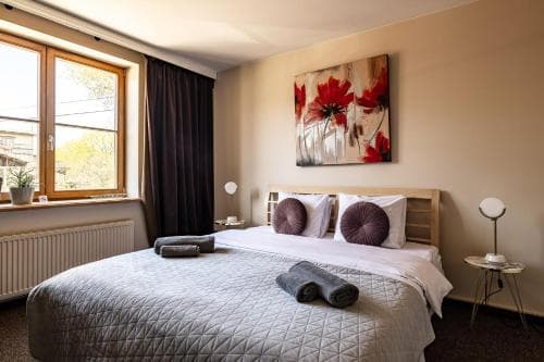 A cozy hotel room features a neatly made bed with rolled towels, vibrant floral artwork on the wall, and a sunny window view, ideal for travelers seeking comfort and relaxation.