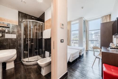 A modern studio apartment features an open-plan layout with a sleek bathroom, cozy bed by a large window with city views, and vibrant red accents, ideal for urban travelers seeking comfort and style.